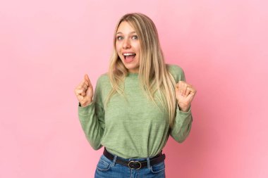 Pembe arka planda izole edilmiş genç sarışın kadın galibiyeti kutluyor.