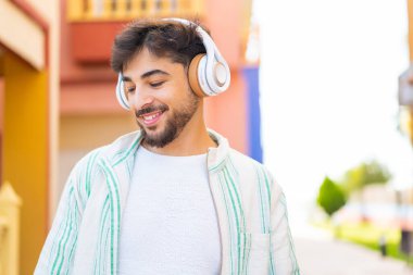 Açık havada müzik dinleyen yakışıklı bir Arap.