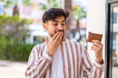 Yakışıklı bir Arap 'ın dışarıda cüzdanı var. Şaşırmış ve şok olmuş bir yüz ifadesi var.
