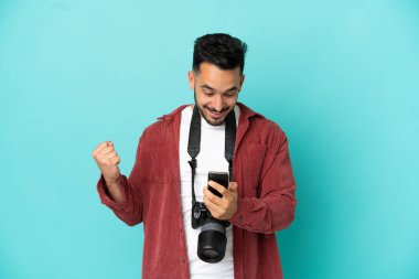 Young photographer caucasian man isolated on blue background surprised and sending a message