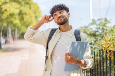Açık havada genç bir Arap öğrencinin kuşkuları ve kafa karıştırıcı bir yüz ifadesi var.