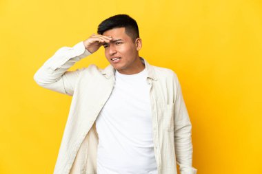 Genç Ekvador 'lu adam sarı arka planda izole edilmiş. Bir şeye bakmak için uzaklara bakıyor.