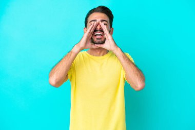 Kafkasyalı genç adam mavi arka planda izole edilmiş bağırıyor ve bir şeyler söylüyor.