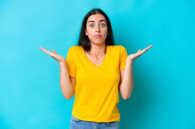 Mavi arka planda izole edilmiş genç beyaz kadın şüpheli hareketler yapıyor.