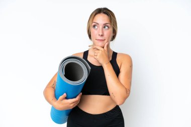 Young caucasian woman going to yoga classes while holding a mat isolated on white background having doubts and thinking