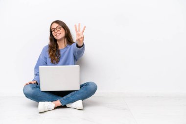 Yerde dizüstü bilgisayarı olan, beyaz arka planda izole edilmiş beyaz bir kadın mutlu ve parmakları olan üç kişi sayıyor.