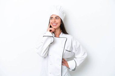 Beyaz arka planda genç aşçı kadın yukarı bakarken bir fikir düşünüyor.