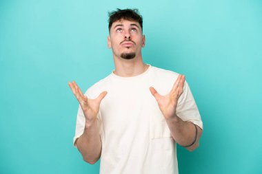 Mavi arka planda izole edilmiş beyaz, yakışıklı genç bir adam bunalımda.