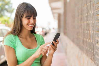 Dışarıdaki genç kadın cep telefonuyla mesaj ya da e-posta yolluyor.