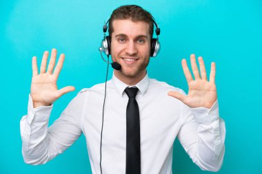 Tele pazarlamacı beyaz adam mavi arka planda izole edilmiş bir kulaklıkla çalışıyor. Parmaklarıyla 10 kişi sayıyor.