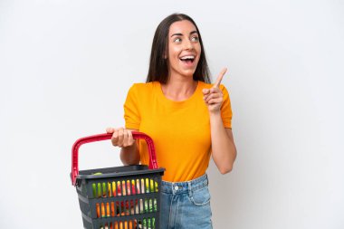 Beyaz arka planda izole edilmiş yiyecek dolu bir alışveriş sepeti tutan beyaz bir kadın çözümü fark ederken parmağını kaldırmayı amaçlıyor.