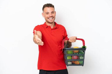 Beyaz arka planda izole edilmiş bir sepet dolusu yiyecek tutan beyaz bir adam iyi bir anlaşma için el sıkışıyor.