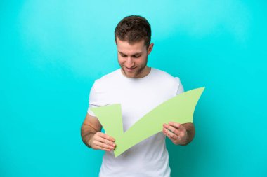 Kafkasyalı genç adam mavi arka planda izole edilmiş. Elinde bir çek simgesi var ve ona bakıyor.