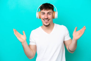 Kafkasyalı yakışıklı adam mavi arka planda izole edilmiş şaşırmış ve müzik dinliyor.