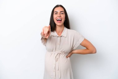 Beyaz arka planda izole edilmiş genç beyaz kadın hamile ve ön tarafı işaret ediyor.