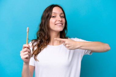 Dişlerini fırçalayan beyaz bir kadın mavi arka planda izole edilmiş ve onu işaret ediyor.