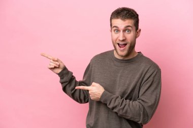 Pembe arka planda izole edilmiş genç beyaz adam şaşırmış ve işaret ediyor.