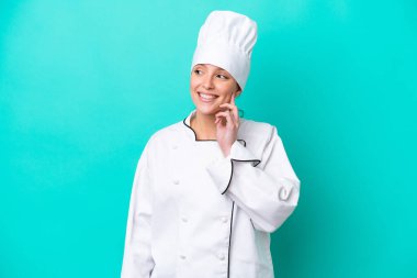 Kafkasyalı genç aşçı kadın mavi arka planda izole edilmiş bir şekilde yukarı bakarken bir fikir düşünüyor.