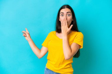 Mavi arka planda izole edilmiş beyaz bir kadın, sürpriz bir ifadeyle işaret ederken...