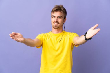 Mor arka planda soyutlanmış yakışıklı sarışın adam sunar ve davet eder.