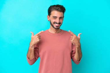 Kafkasyalı genç adam mavi arka planda izole edilmiş bir şekilde baş parmak işareti yapıyor.