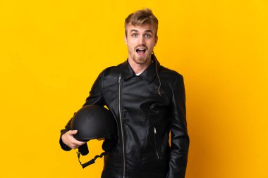 Motosiklet kasklı bir adam sarı arka planda izole edilmiş, şaşırmış bir yüz ifadesi var.