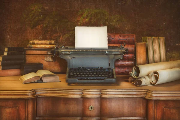Old wooden desk with vintage typewriter holding an empty sheet of paper and ancient books and maps