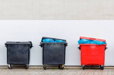 Bir duvarın önünde fotokopi alanı olan üç endüstriyel Hollanda atık konteynırı.
