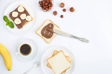 Beyaz arka planda çikolatalı ekmek, muz ve kahve fincanının üst görüntüsü. Boşluğu kopyala.