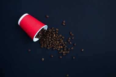 Siyah arka planda kahve çekirdekleri olan tek kullanımlık kırmızı kağıt bardak. Üst Manzara. Boşluğu kopyala.