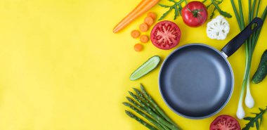 Empty metal frying pan and vegetables on the yellow background. Copy space.Top view.