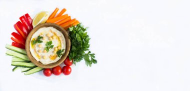 Hummus in the brown bowl and vegetable on the white background. Top view. Copy space.