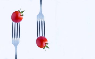 Cherry tomato stabbed on a silver fork on the white background. Close-up. Copy space.