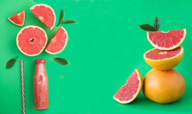 Cam şişede greyfurtlu smoothie ve yeşil arka planda dengede duran greyfurt piramidi. Yakın plan. Boşluğu kopyala.