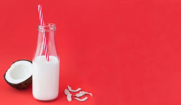 Coconut milk in the glass bottle on the red background. Close-up. Copy space.