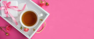 Beyaz fincanda çay ve pembe arka planda beyaz ahşap tepside hediye kutusu. Boşluğu kopyala. Üst görünüm.