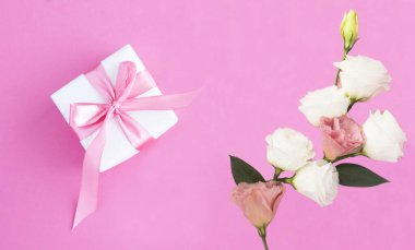 Pembe fiyonklu bir hediye kutusu ve pembe arka planda çiçekler. Uzayı kopyala Üst görünüm.