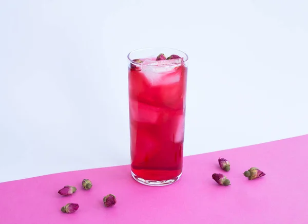 Pink cocktail with ice and rose flower in the drinking glass on the colored background. Close-up.