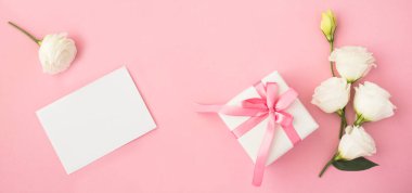Mesaj için boş beyaz kağıt, hediye kutusu ve pembe arka planda güzel beyaz çiçekler. Üst Manzara. Boşluğu kopyala.