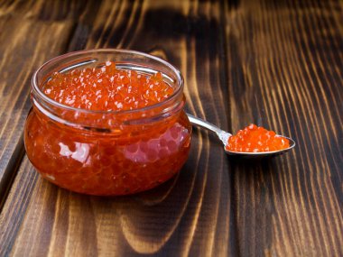 Ahşap arka plandaki cam kavanozda kırmızı havyar. Yakın plan..