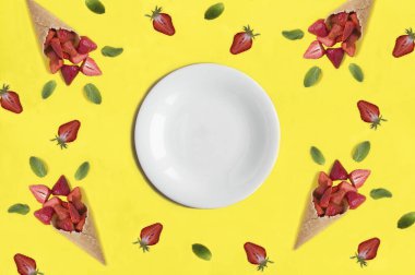 Mesaj için boş beyaz tabak ve sarı arka planda çilekli dondurma külahı. Uzayı kopyala Üst görünüm.