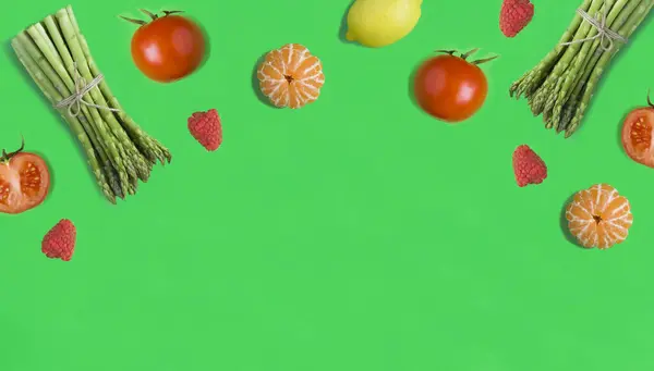 Lemon, raspberry, asparagus, tomato and tangerine on the green background. Copy space. Top view.