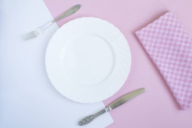 Boş beyaz tabak, pembe arka planda bıçak ve çatal. Uzayı kopyala Üst görünüm.