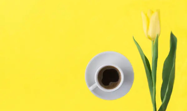 Coffee cup and yellow tulip on the yellow  background. Top view. Copy space.