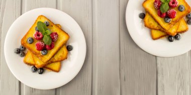 Gri ahşap arka planda beyaz tabakta böğürtlenli tost ve bal. Üst Manzara. Boşluğu kopyala.