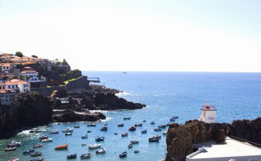 Beautiful view of the ocean, city, colored boats and lighthouse on a summer day. Camara de Lobos. Madeira. Portugal. clipart