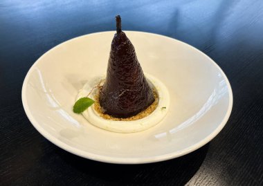 Siyah ahşap zemin üzerinde beyaz bir tabakta karamelize armut. Yakın plan..