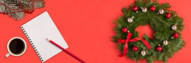 Noel çelengi, not defteri ve kırmızı arka plandaki beyaz fincanda siyah kahve. Uzayı kopyala Üst görünüm.