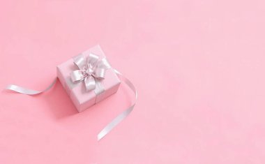 Pembe arka planda bağlı bir fiyonklu pembe hediye kutusu. Üst Manzara. Boşluğu kopyala.