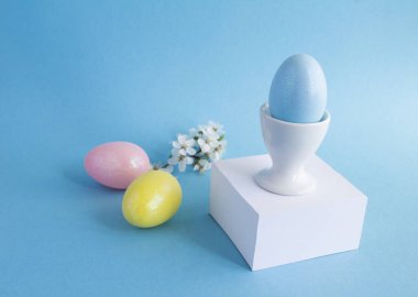 Mavi arka plandaki beyaz küpün üzerindeki beyaz yumurta kabında mavi paskalya yumurtası. Yakın plan..